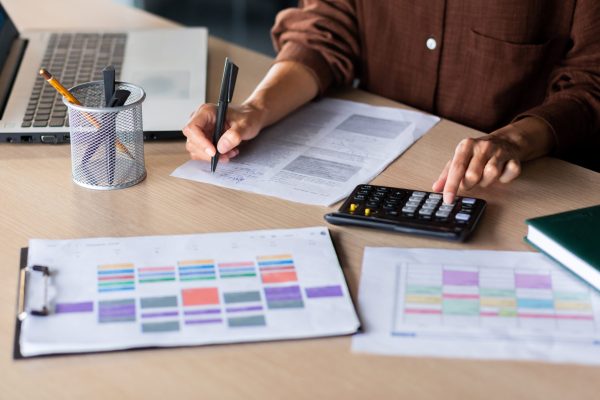 Close-up photo. Female hands of an accountant, auditor, financier, banker working in the office at a table with documents and with a laptop, using a calculator.